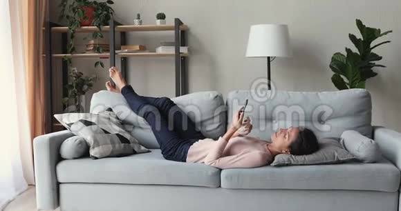 躺在沙发上用智能手机放松的年轻女子视频的预览图