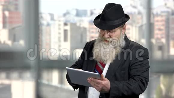 使用平板电脑穿深色西装的长胡子老人视频的预览图