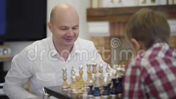 快乐白种人和儿子下棋的肖像微笑聪明的父亲在家教育孩子家庭视频的预览图