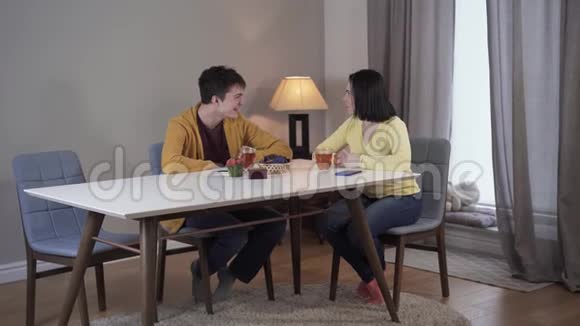 长镜头的快乐白种人十几岁的儿子和成年母亲坐在桌子旁交谈微笑的女人和男孩视频的预览图