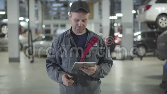 镜头接近男性汽车机械师拿着平板电脑并显示汽车钥匙在相机微笑成年白种人视频的预览图