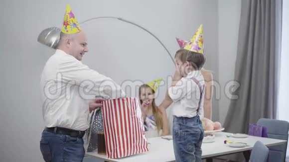 镜头接近可爱的小男孩戴着派对帽收到玩具车为他的生日带礼物的快乐孩子视频的预览图