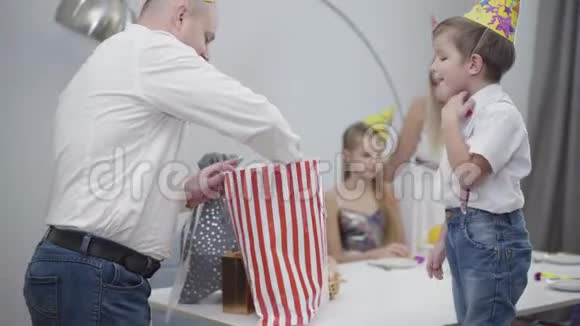 成年白种人戴着派对帽赠送儿子玩具车作为生日礼物的肖像快乐的父亲拿出玩具和视频的预览图