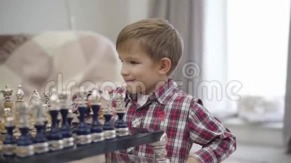 特写可爱的白种人男孩坐在棋盘前微笑聪明的孩子在室内享受他的爱好视频的预览图