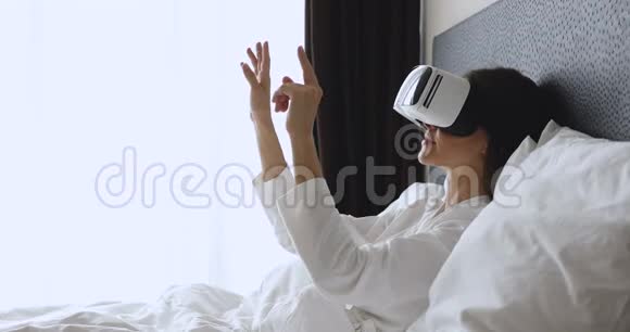 年轻女子戴着虚拟现实眼镜躺在床上视频的预览图