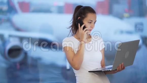 女人用手机和笔记本电脑在机场工作背景模糊的飞机视频的预览图