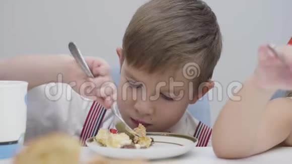 小白种人男孩吃美味蛋糕的特写可爱的孩子坐在桌子旁享受甜食视频的预览图