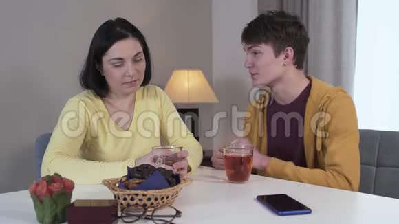 自信的十几岁白人男孩和母亲坐在桌子旁交谈的肖像成年黑发女人喝酒视频的预览图