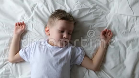可爱的小男孩蹒跚学步醒来在卧室的床上打哈欠和伸展关门视频的预览图