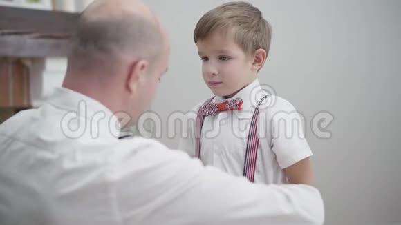 后景为成年白种人男子化妆子年轻的父亲给小男孩穿上优雅的衣服说话支助视频的预览图