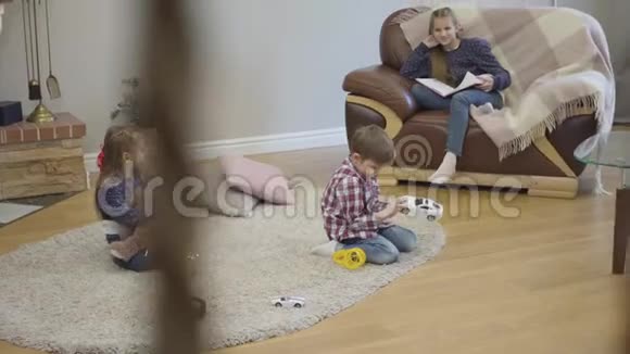 三个白人孩子坐在家里聊天小女孩和男孩拿着玩具当他们十几岁的妹妹坐在上面视频的预览图