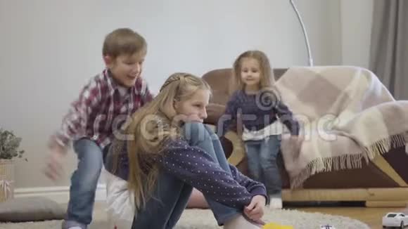 小白种人女孩和男孩跑到姐姐坐在地毯上拥抱她友好兄弟姐妹的肖像视频的预览图