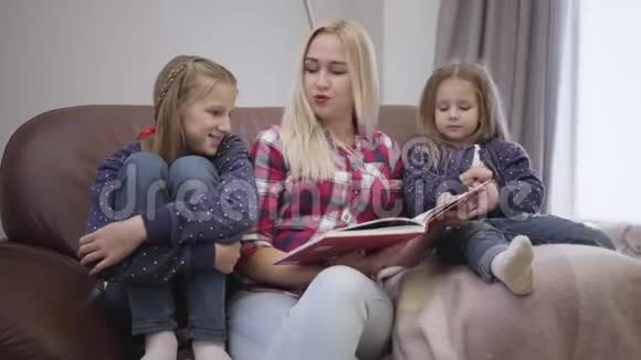 一幅美丽的高加索女人和女儿坐在沙发上看书的肖像母亲在家教育孩子视频的预览图
