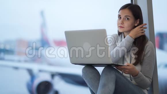 女人在笔记本电脑上工作看镜头笑背景上模糊的飞机视频的预览图