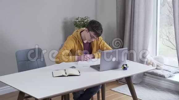 青少年白种人黑发男孩做家庭作业的俯视图英俊聪明的大学生在室内努力学习视频的预览图