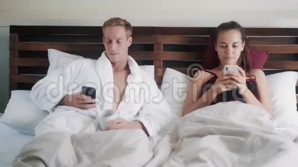 一对夫妇早上躺在床上男人打电话女人上网聊天视频的预览图