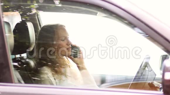 年轻漂亮的女孩坐在车轮旁用手机说话视频的预览图