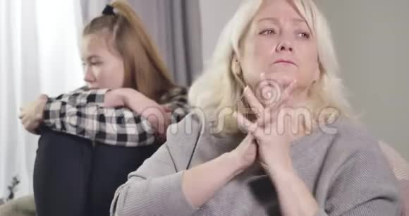 一位忧心忡忡的白种人祖母抬起头来握手令人不安的十几岁孙女坐着视频的预览图