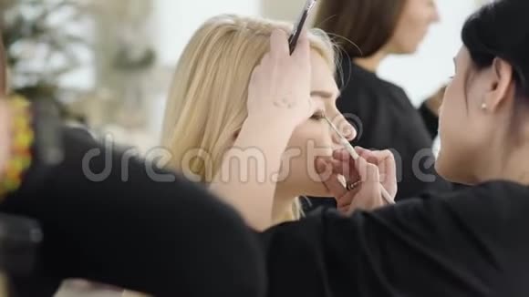 在美容院化妆的金发白种人女人的近景女性面部用眼线涂抹视频的预览图