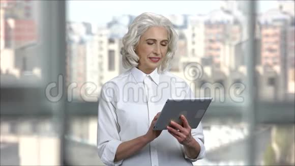 头发灰白的女商人在办公室里使用数字平板电脑视频的预览图