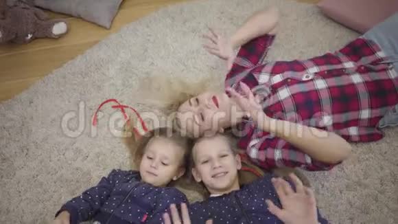镜头接近年轻的白种人母亲躺在柔软的地毯上双手举起开朗的家庭视频的预览图