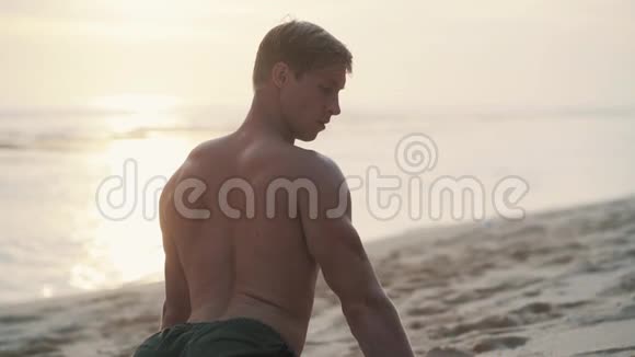 肌肉发达的人在日落时在海滩上做瑜伽练习动作缓慢视频的预览图