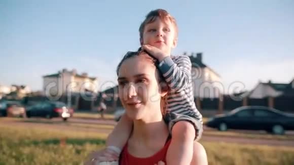 妈妈和儿子在一起可爱的小男孩坐在妈妈的肩膀上她开心地笑着阳光明媚慢节奏视频的预览图