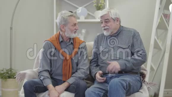 积极的高白种人伴侣聊天开玩笑和拥抱两个老人坐在养老院的沙发上退休人员视频的预览图