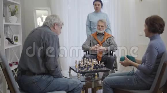 年轻女性志愿者在养老院照顾三名退休人员年长的白人男子下棋老妇人视频的预览图