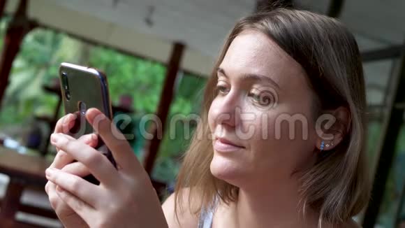 美丽的女人夏天在家附近使用智能手机视频的预览图