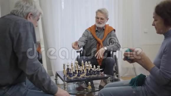 自信的老人戴着眼镜在养老院里和同伴下棋就像老妇人在旁边编织一样视频的预览图