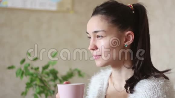 一个年轻迷人的女孩在家里坐在床上时喝着粉红色杯子里的咖啡视频的预览图