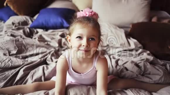 可爱的女婴金发在床上坐在分裂和微笑快乐的孩子慢动作在斯塔迪加姆射击视频的预览图