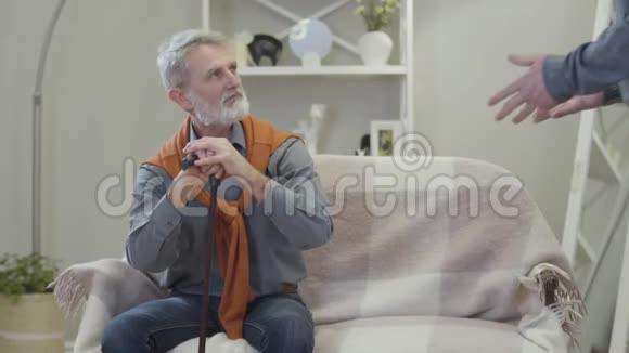 英俊的白人老人在室内问候朋友快乐的男性退休者拥抱坐在沙发上的家伙视频的预览图