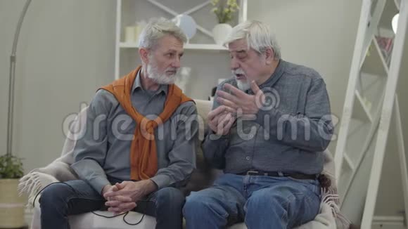 两个白人老人在疗养院谈话的肖像成熟的男性退休人员坐在沙发上聊天视频的预览图
