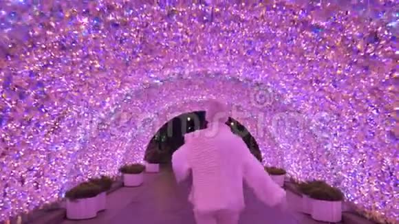 穿着白色毛衣和帽子的女人在夜晚穿过粉红色发光的隧道视频的预览图