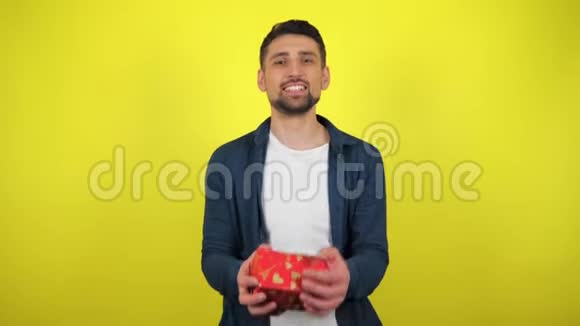 一个穿着白色T恤的年轻人拿着一个盒子手里拿着一件礼物看着相机微笑着黄色的背景视频的预览图