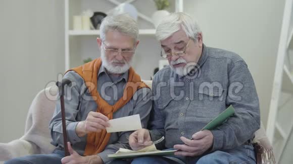 白人老人在室内观看黑白照片的肖像老年男性退休朋友分享回忆视频的预览图