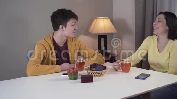 开朗的白人母亲和十几岁的儿子坐在家里的桌子上谈笑风生的肖像友好快乐视频的预览图