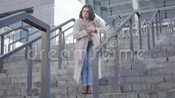 布鲁内特白种人女商人站在楼梯上双手放在胸前年轻女子突然对城市感到心痛视频的预览图