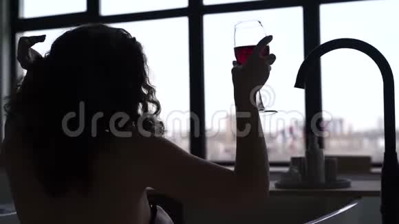 年轻开朗的女人在浴缸里喝红酒一个棕色卷发的白人女孩在洗澡时在前面放松视频的预览图