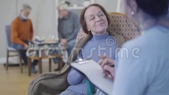微笑成熟的白种人女人编织和手势是的摇着头作为志愿者问她的问题快乐的老人视频的预览图