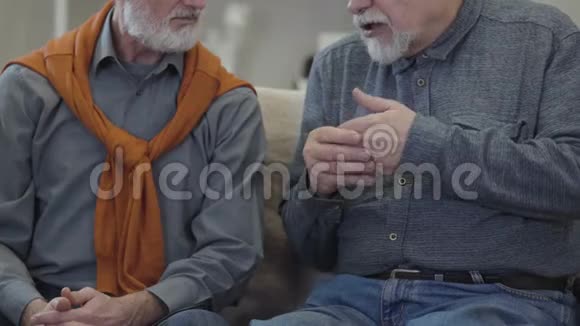 无法辨认的老白种人与朋友交谈和手势两名男性退休人员坐在沙发上聊天视频的预览图