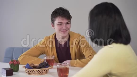 带着微笑的白种人黑发男孩和母亲谈话的肖像就像坐在桌子旁喝茶和吃糖果一样积极正面视频的预览图