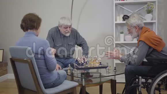 成熟的白发白种人男子下棋和说话女人在扶手椅上编织老年病人和残疾人视频的预览图