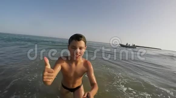微笑的男孩伸出大拇指在大海中奔跑视频的预览图