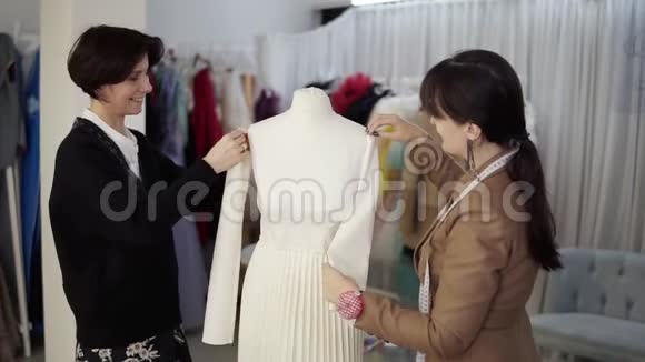 女专业裁缝设计人员在工作室的人体模型上设计新的白色服装视频的预览图