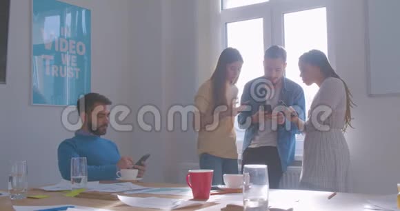 四位不同种族的同事在办公室喝咖啡休息时间使用智能手机现代互联网问题视频的预览图