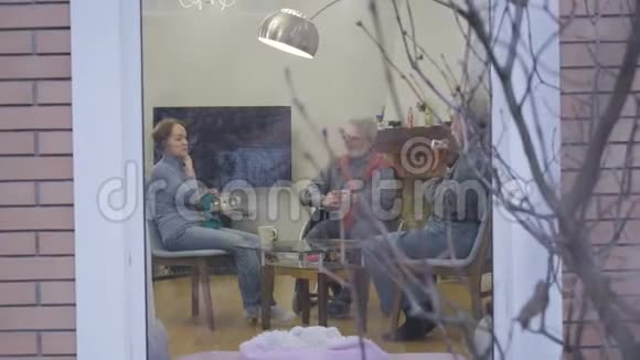 三个白人老人在养老院聊天喝茶男人和女人在室内度过安静的夜晚视频的预览图