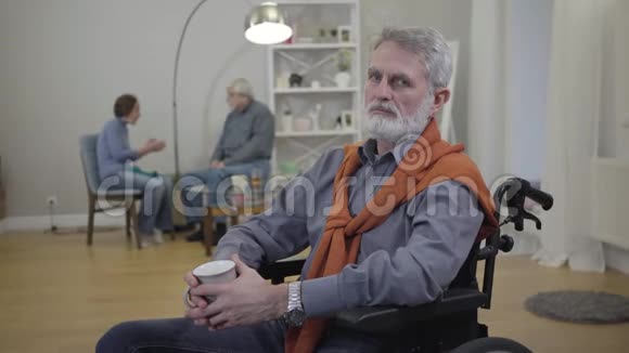 英俊的老白种人坐在轮椅上看镜头的肖像老年男性退休人员开支视频的预览图